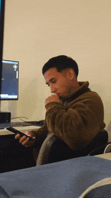 a man sitting in front of a computer looking at a cell phone