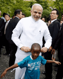 a boy wearing a blue shirt that says nautica is being held by a man in a white shirt