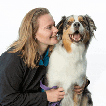 a woman in a black jacket is holding a brown and white dog