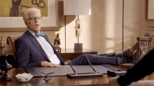 a man in a suit and bow tie is sitting at a desk with his feet up on the desk .