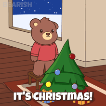 a teddy bear standing next to a christmas tree with the words it 's christmas