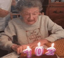 an elderly woman is blowing out candles on a cake .