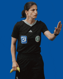 a woman wearing a black adidas shirt is holding a banana to her ear