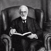 a man in a suit is sitting in a chair reading a book and holding a pen