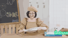 a woman sits at a table with a box of plastic wrap in front of a chalkboard that says smile