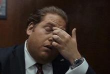 a man wearing a suit and tie is rubbing his eyes