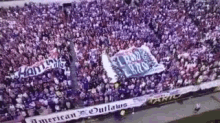 a large crowd of people are standing in a stadium with a banner that says `` american outlaws '' on it .