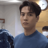 a man in a blue shirt is looking at the camera with a clock in the background that shows the time as 10:13