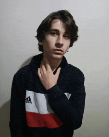 a young man wearing an adidas sweater holds his hand to his chin