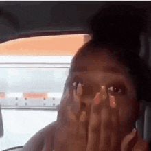a woman with long nails is sitting in a car covering her face with her hands .