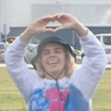 a woman is making a heart shape with her hands while wearing a hat .