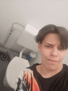 a young man taking a selfie in a bathroom with a toilet in the background