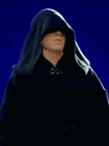 a man wearing a black hooded cape is standing on a blue background .