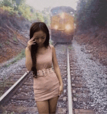 a woman in a pink dress standing on train tracks