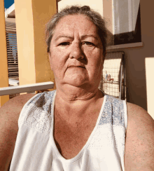 a woman in a white tank top is sitting on a balcony looking at the camera