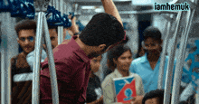 a man in a red shirt is holding onto a railing on a train with iamhemuk written on the bottom right