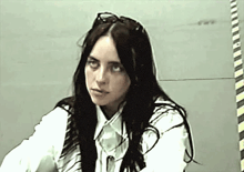 a woman with long black hair and glasses is wearing a white shirt and a vest .