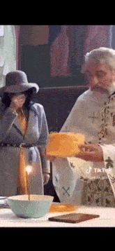 a woman in a hat is covering her face while a priest holds a piece of bread in front of her .