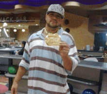 a man in a striped shirt is holding a gold medal in front of a sign that says nack bar