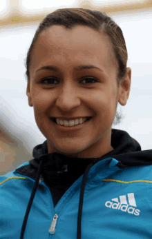 a woman in a blue adidas jacket smiles for the camera