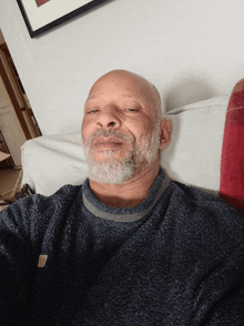 a bald man with a beard is sitting on a white couch