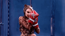 a woman in a leopard print costume is wearing red boxing gloves and a cat mask .