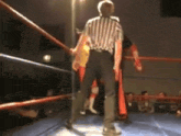 a referee in a striped shirt is standing in a wrestling ring with two wrestlers
