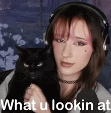 a woman with headphones is holding a black cat .