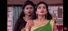 two women are standing next to each other and one of them is wearing a green saree