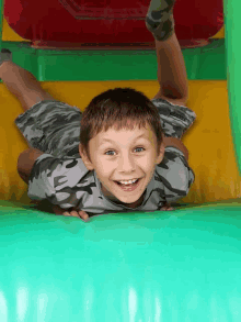 a boy in a camo shirt is laying on a green and yellow inflatable slide