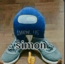 a blue among us stuffed animal is sitting on top of a pair of shoes and giving a thumbs up .