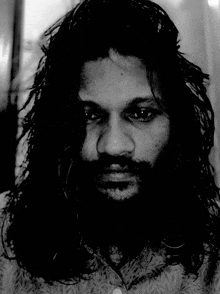 a man with long hair and a beard looks at the camera in a black and white photo