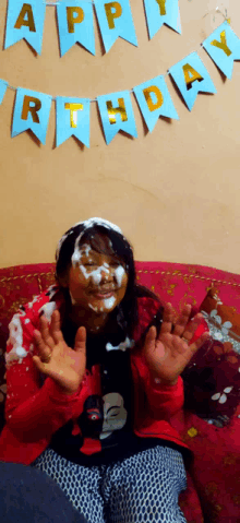 a girl with whipped cream on her face is sitting on a couch with a happy birthday banner behind her