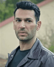 a man wearing a leather jacket and a black shirt looks at the camera