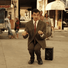 a man in a suit and tie is kneeling down in front of a speaker