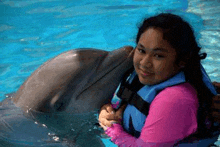 a young girl is holding a dolphin in a pool .