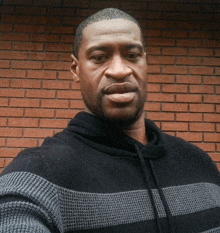 a man wearing a black and gray striped sweater stands in front of a brick wall