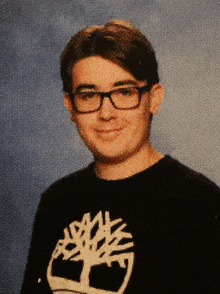 a young man wearing glasses and a timberland shirt poses for a picture