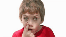 a young boy in a red shirt is picking his nose with his finger .