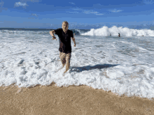 a man in a black shirt is running in the water on a beach