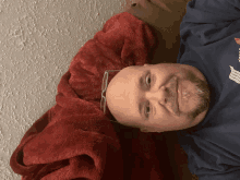 a man wearing glasses is laying on his back with a red blanket around his head