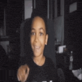 a young boy in a black shirt is giving a peace sign while sitting in a chair .