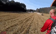 a man in a red shirt with the word en on his back is watching a group of atv riders in a field .