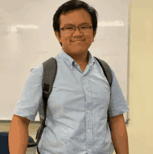 a man wearing glasses and a blue shirt is standing in front of a white board