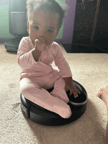 a baby in a pink outfit is sitting on a vacuum