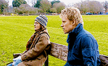 a man and a woman are sitting on a bench in a park . the woman is wearing a striped hat .