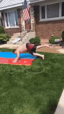 a man is doing push ups on a water slide in front of a house with an american flag in the background