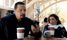 a man and a woman sit at a table looking at their cell phones with a speed limit sign in the background