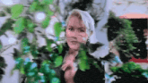 a woman in a black jacket is standing in front of a tree with green leaves .