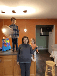 a woman stands in a kitchen with two children